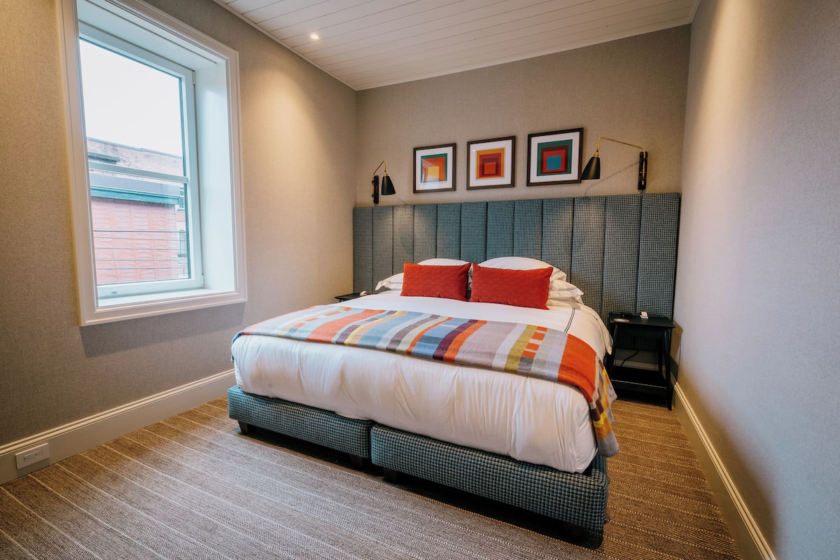 Une chambre à coucher avec un grand lit, une fenêtre et une tête de lit ornée d’œuvres d’art.