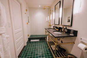 A bathroom with a green tiled floor, two sinks with gold fixtures, a towel rack, and a mirror. - Eleven Revelstoke Lodge (Revelstoke)