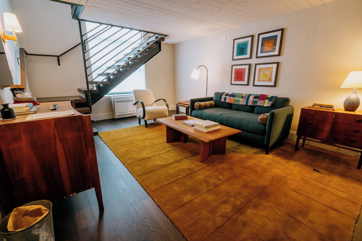 Un salon avec un bureau en bois, un canapé vert, une table basse en bois et un escalier.
