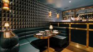A bar area with a geometric patterned wall, a bar counter with glasses and bottles, and a booth seating area with a table and lamps. - Eleven Revelstoke Lodge (Revelstoke)
