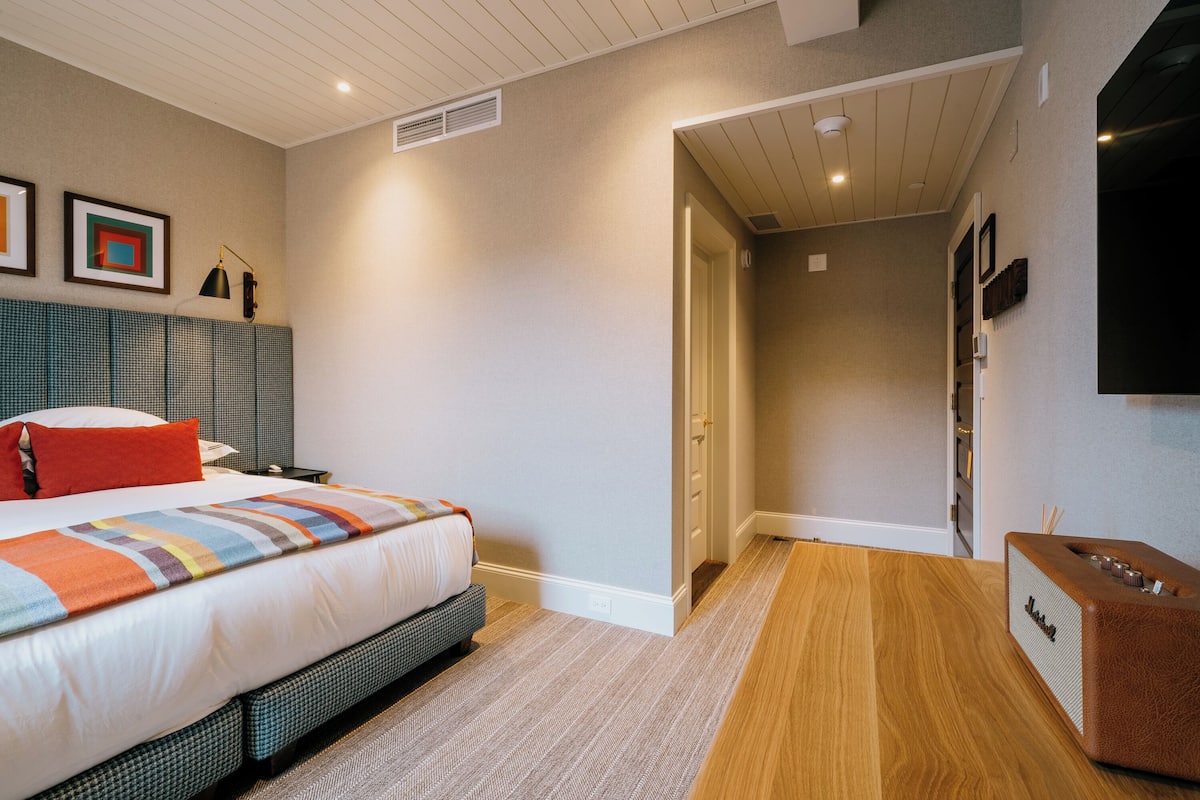 Une chambre à coucher comprenant un lit, une table de chevet, une lampe, un haut-parleur et un téléviseur fixé au mur.