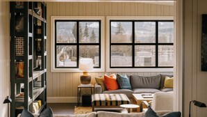 A cozy living room with a large window, a bookshelf, a sofa with cushions, and a small table with a lamp. - Eleven Revelstoke Lodge (Revelstoke)