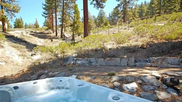 Un bain à remous installé dans un cadre naturel, avec un mur de pierres et des arbres en arrière-plan.