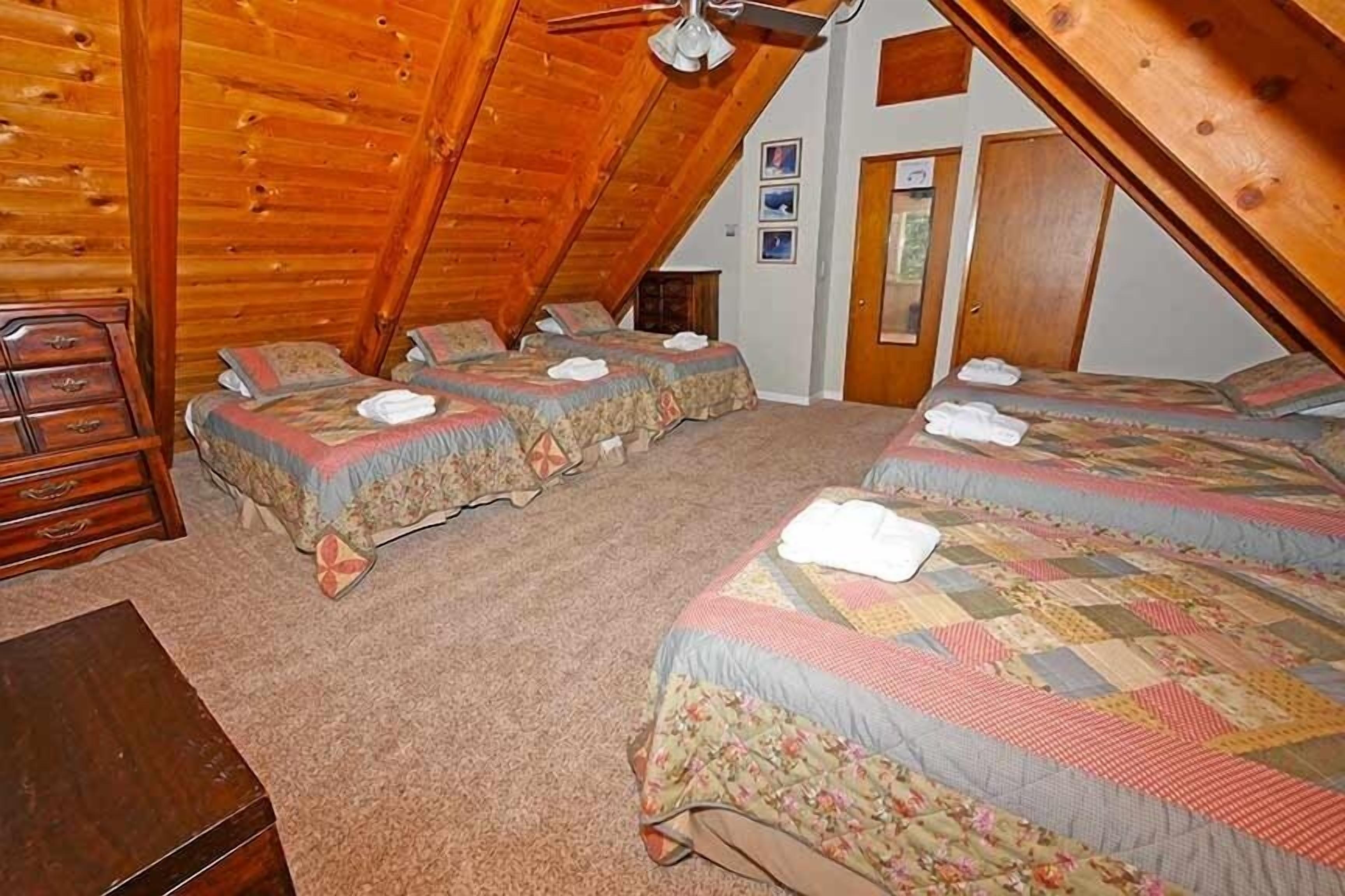 Un dormitorio abrigado en el ático, con tres camas, paredes de madera y un ventilador de techo.