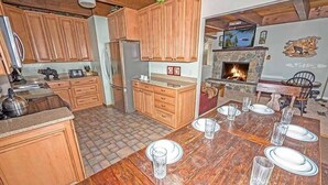 A wooden kitchen with a dining table set for six, a stone fireplace, and wooden cabinets. - 3542 Bobby Grey Circle 3 Bedroom Cabin by RedAwning (South Lake Tahoe)