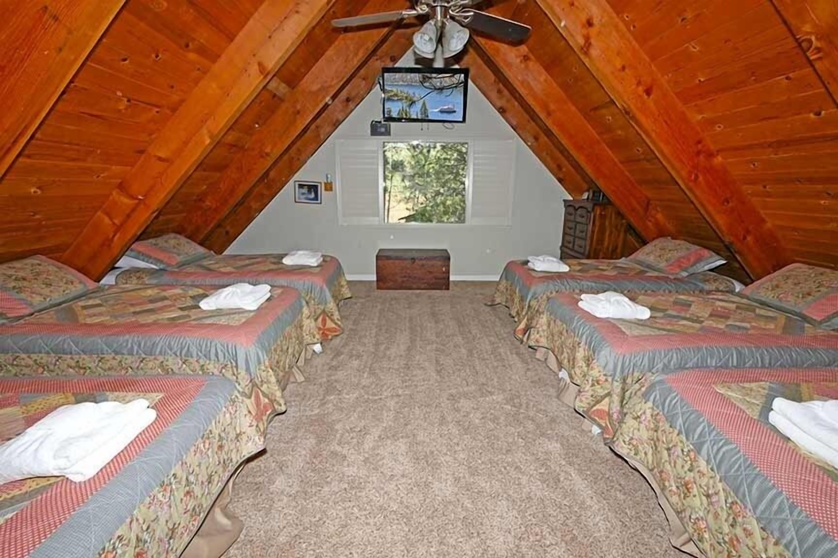 Une chambre confortable située sous les toits, avec deux lits, un ventilateur de plafond et une fenêtre donnant sur les arbres.