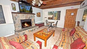 A cozy living room with a stone fireplace, patterned sofas, a coffee table, and a dining area with chairs. - 3542 Bobby Grey Circle 3 Bedroom Cabin by RedAwning (South Lake Tahoe)