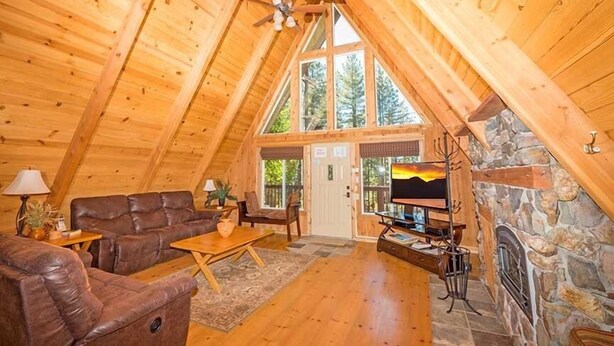 Un acogedor espacio tipo loft con techo de madera, chimenea de piedra, sofá de cuero y televisor.
