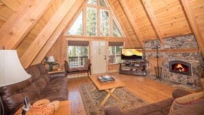Un acogedor loft con chimenea de piedra, vigas de madera, sofá de cuero y televisor.