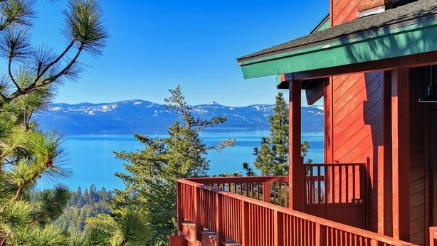 Une cabane en bois rouge dotée d’un balcon donnant sur un lac et des montagnes.