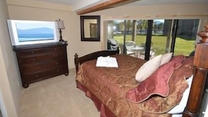 A bedroom with a bed, a dresser, a TV, and a view of the outdoors.
