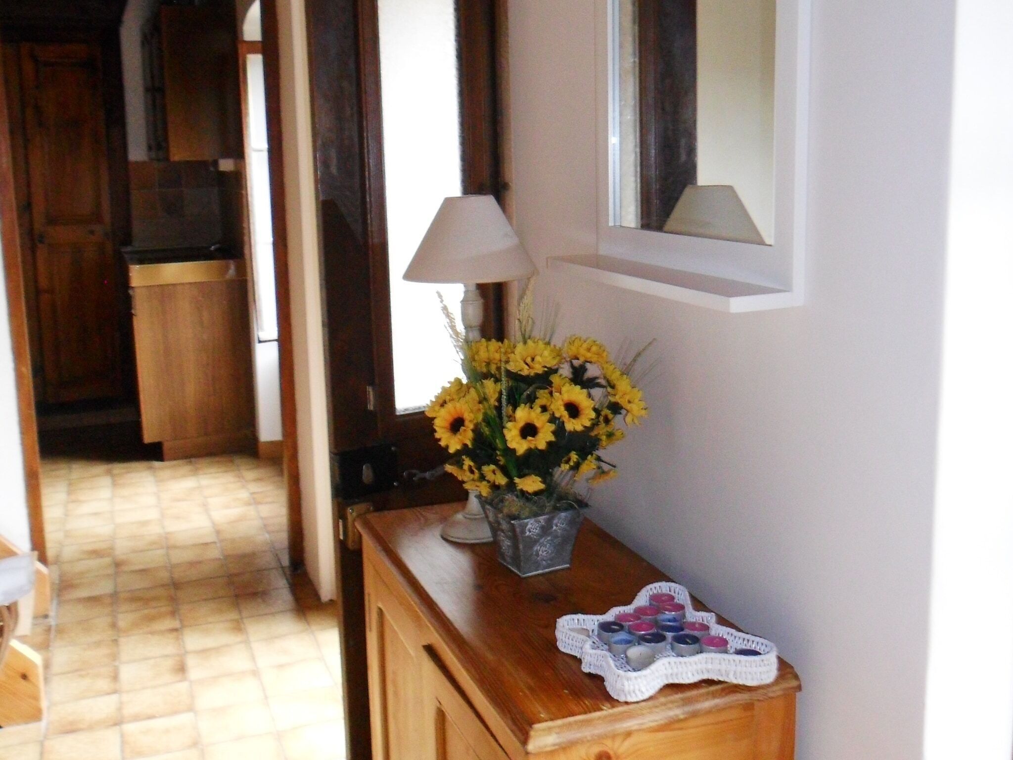 Un pasillo con un armario de madera, un jarrón de flores amarillas y una lámpara en la pared.