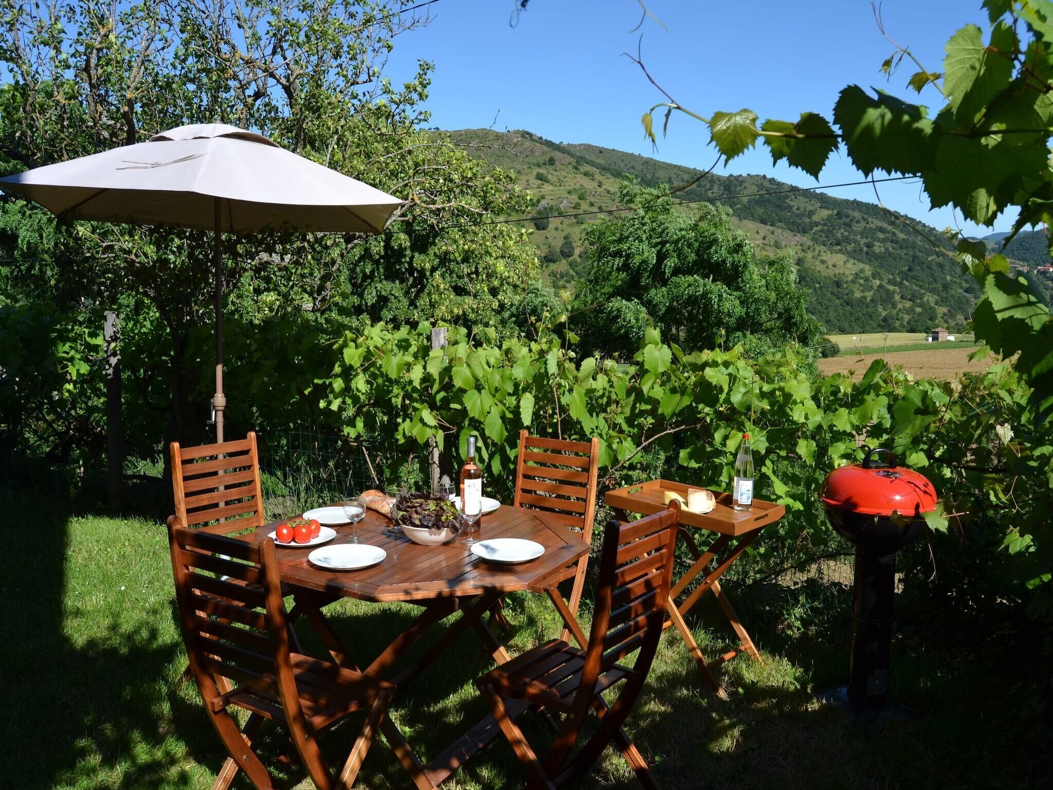 An outdoor dining area with a wooden table and chairs, a wine bottle, and a grill.