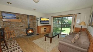 A living room with a stone wall, fireplace, TV, and a view of the outdoors.