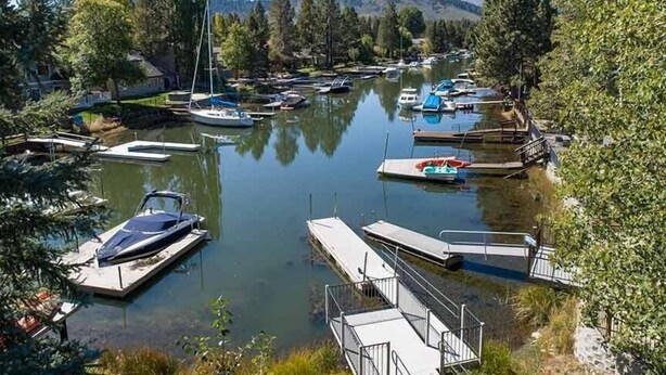 A marina with boats docked, surrounded by trees and a mountainous backdrop.