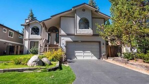 A two-story house with a garage, a front yard with a lawn and a small tree, and a wooden fence.