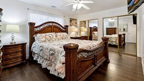 Une chambre à coucher avec un lit en bois, deux tables de chevet, un ventilateur de plafond et un grand miroir.