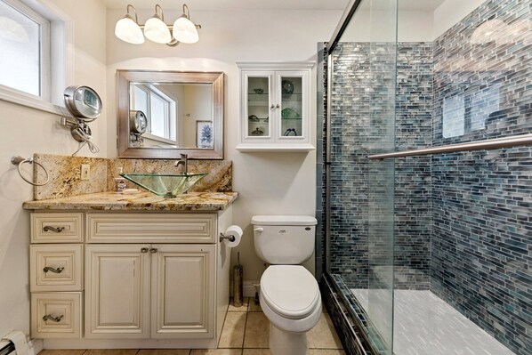 A bathroom with a glass shower enclosure, a marble sink, a toilet, and a cabinet with a mirror. - 917 Tahoe Keys Blvd by RedAwning (South Lake Tahoe)