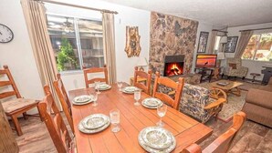 A dining area with a wooden table set for six, surrounded by wooden chairs. A stone fireplace with a TV is in the background. - 948 Merced Avenue 3 Bedroom Home by RedAwning (South Lake Tahoe)