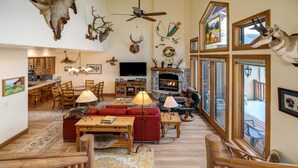 A spacious living room with a fireplace, wooden furniture, and a large window overlooking a deck. - Crosstimbers 2784 3 Bedroom Townhouse by RedAwning (Steamboat Springs)