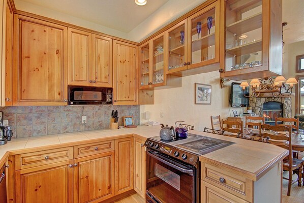 Una cocina con armarios de madera, microondas, horno y comedor con sillas y una mesa.