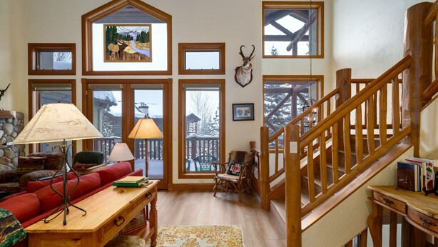 A cozy living room with a red sofa, wooden coffee table, and a staircase with wooden railings. - Crosstimbers 2784 3 Bedroom Townhouse by RedAwning (Steamboat Springs)