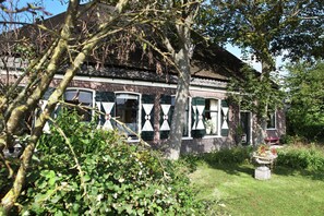 A traditional brick building with multiple windows and a garden area with a small tree and a flower bed.