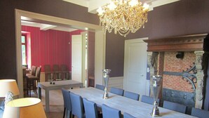 Un espace repas comprenant une longue table, des chaises, un lustre et une cheminée.