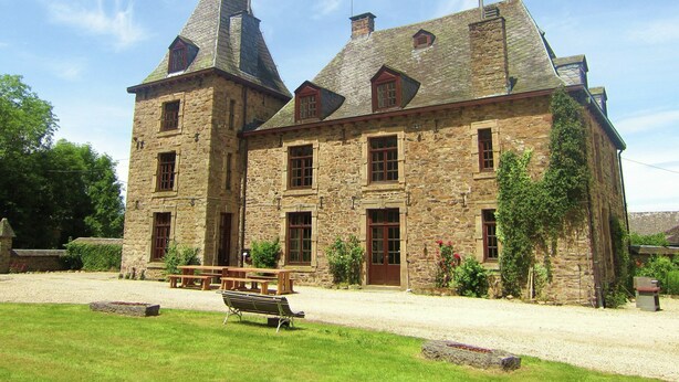 Un bâtiment en pierre doté d’une tour centrale, de nombreuses fenêtres et d’une cour pavée avec des bancs.