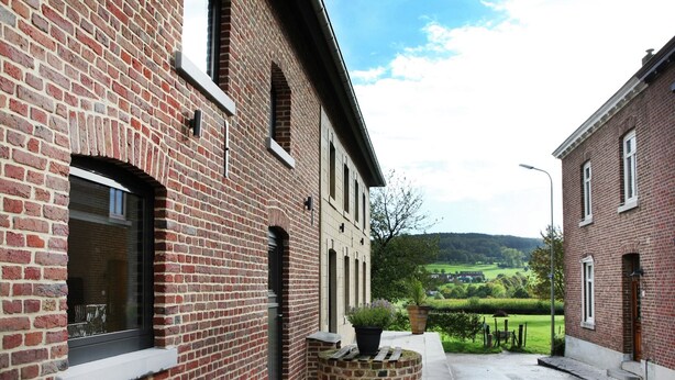 A brick building with a patio area, outdoor seating, and a view of a green landscape.