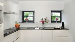 A modern kitchen with white cabinetry, black countertops, and two windows with flower arrangements.