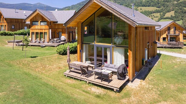 Une cabane en bois dotée d’une grande fenêtre en verre, d’une terrasse et offrant une vue sur les montagnes.