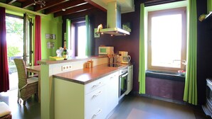 Une cuisine avec un îlot central, un four à micro-ondes et une cuisinière. On y trouve une chaise en osier et une petite table avec une bouteille et un bol.