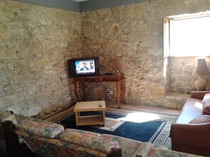 A stone-walled room with a television on a wooden stand, a sofa, and a lamp. - Historical Charming Vintage Villa with 4 bedrooms & country views 4 Villa by RedAwning (Alcobaça)