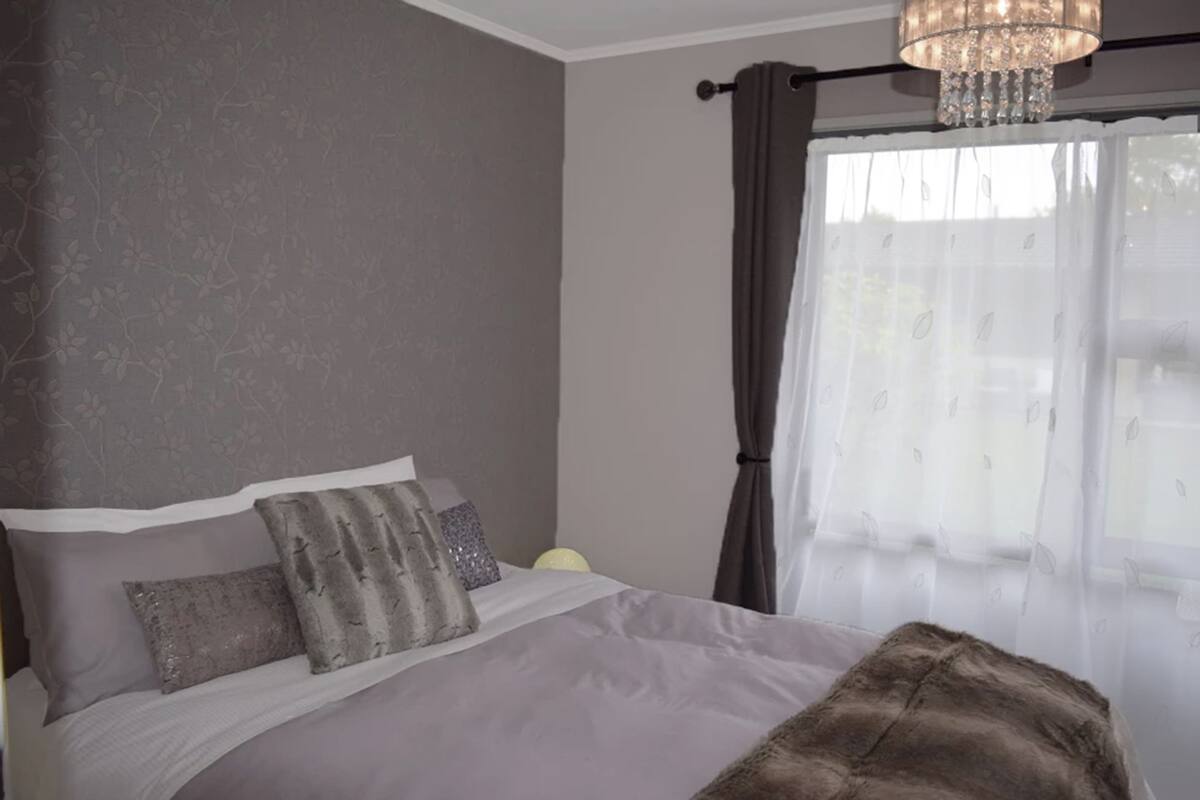 A bedroom with a bed, grey walls, a chandelier, and a window with curtains.