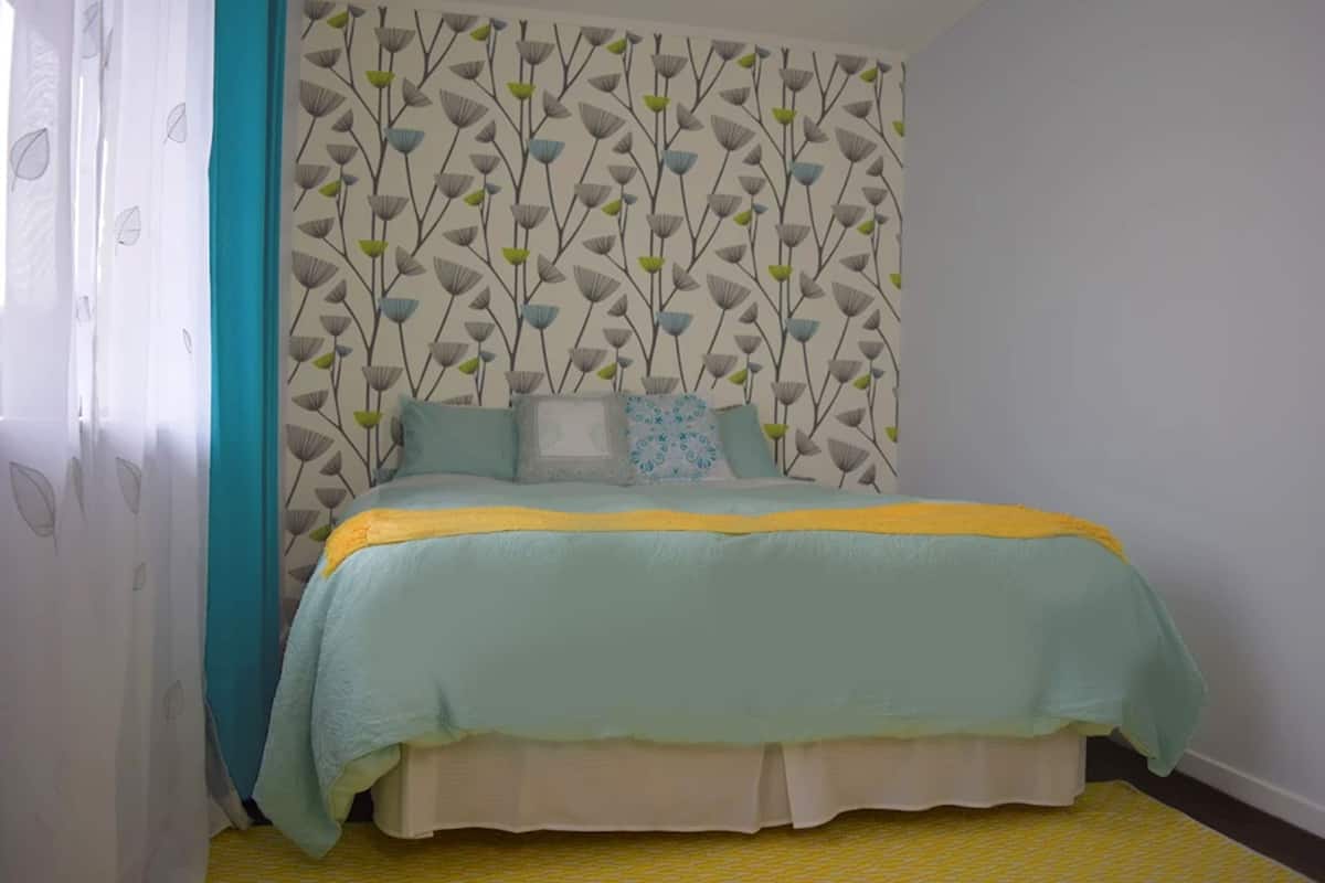 A bedroom with a bed, a patterned wallpaper, and a yellow carpet.