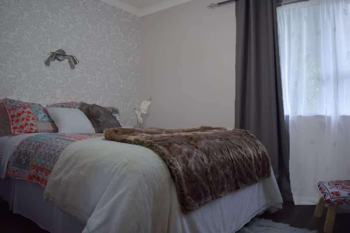 A bedroom with a bed, a decorative wall, a window with curtains, and a small stool.