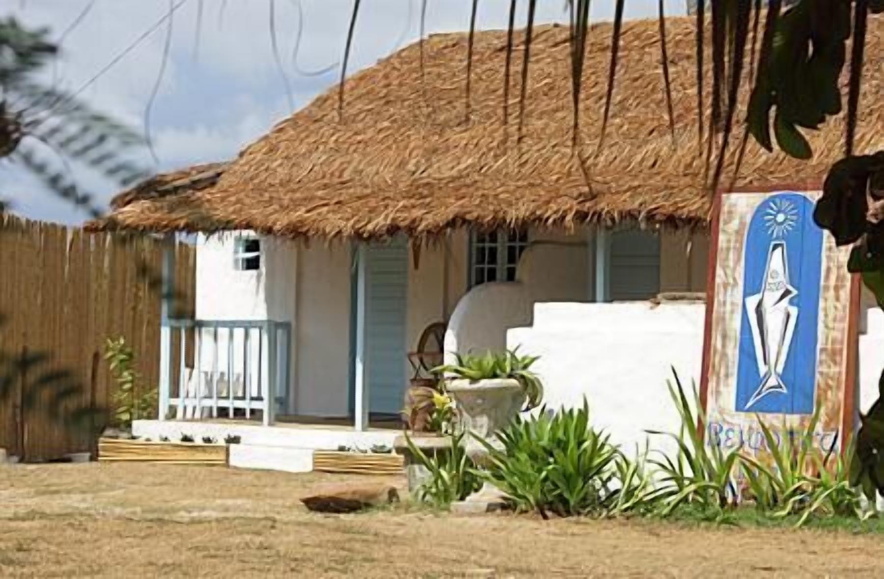 A thatched-roof building with a white exterior, a small porch, and a sign with a religious figure.