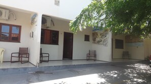 A building with a covered porch, two air conditioning units, and a tree providing shade. - Pousada e Pizzaria Sol e Alegria (Fortaleza)