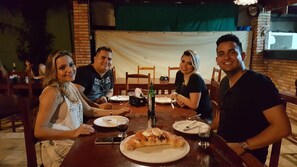 Un groupe de quatre personnes est assis à une table dans un restaurant. On aperçoit, en arrière-plan, un mur de briques et un rideau vert.