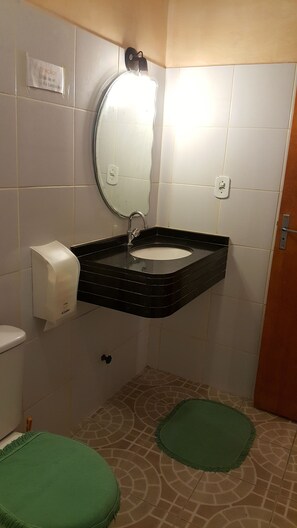 A bathroom with a black sink, white tiles, a mirror, a soap dispenser, and a green rug on the floor. - Pousada e Pizzaria Sol e Alegria (Fortaleza)