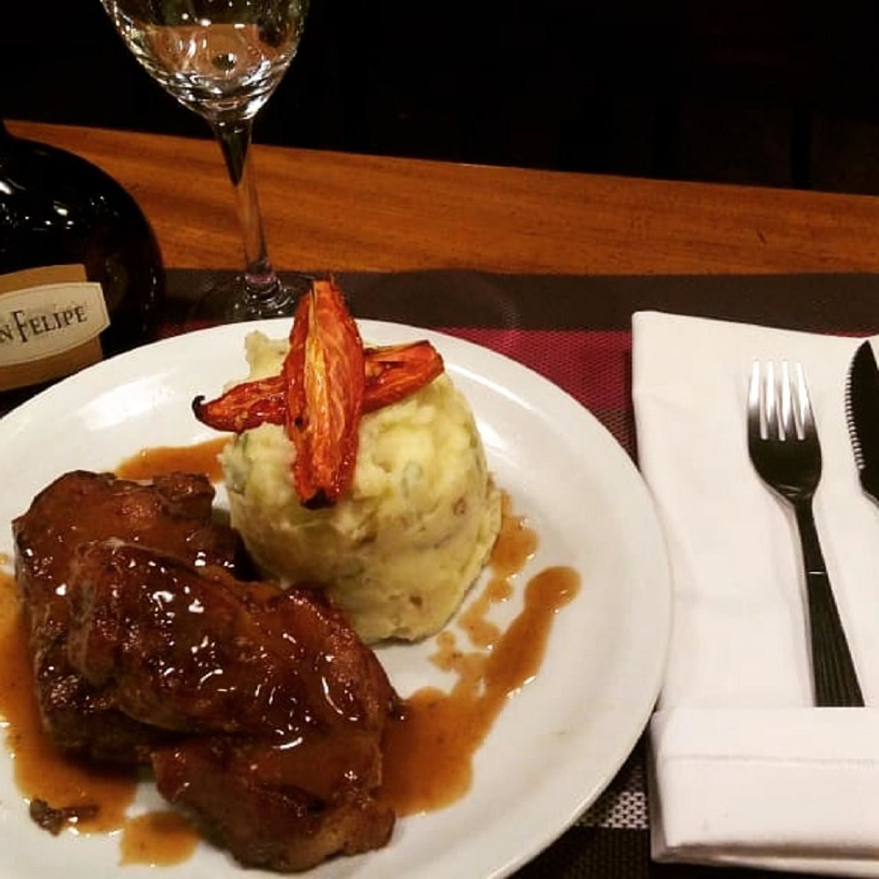 A plate with a steak, mashed potatoes, and gravy, accompanied by a glass of wine.