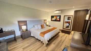 A hotel room with a large bed, bedside tables with lamps, a desk, a wardrobe, and an air conditioning unit.