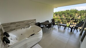 Un baño con una bañera grande, una mesa con sillas y un balcón con vistas a un viñedo.