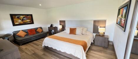 A modern hotel room with a large bed, a sofa, a desk, and a chair.