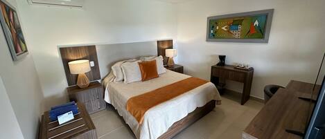 Habitación de hotel con cama, dos mesitas de noche, un escritorio, una silla, un cuadro en la pared y un aire acondicionado.
