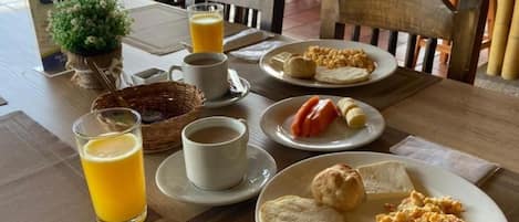 A table set for breakfast with plates of eggs, toast, and biscuits, accompanied by a glass of orange juice and a cup of coffee.