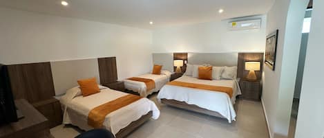 Habitación de hotel con tres camas, un escritorio, una silla y un televisor.