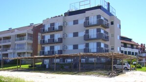 A multi-story residential building with balconies, a covered outdoor area, and a car parked nearby. - Portasol Apart Hotel (Pinamar)