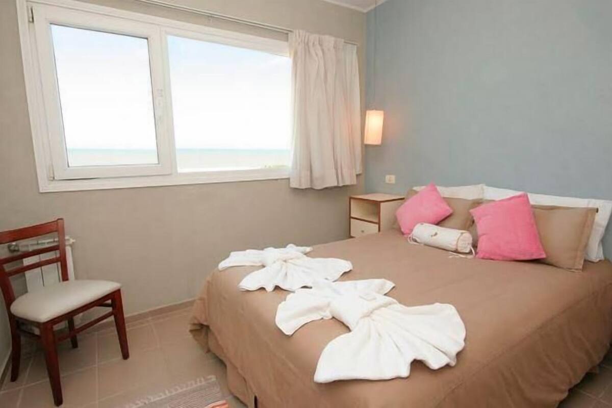 A hotel room with a bed, a chair, a nightstand, and a window with a view.
